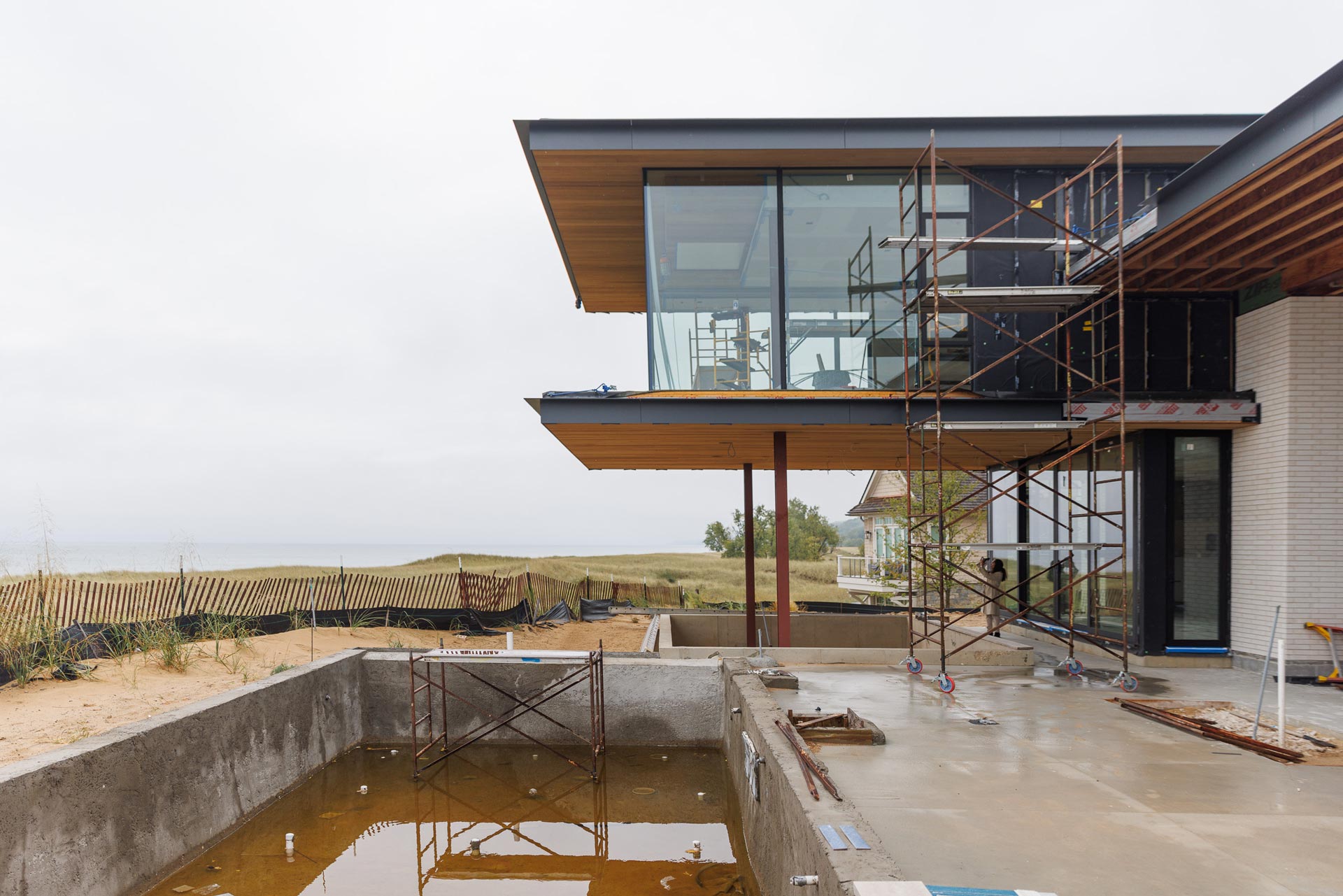 outside view of Northshore Residence with unfinished pool and in construction. Second floor boasts floor to ceiling window walls and is suspended over a lower deck area